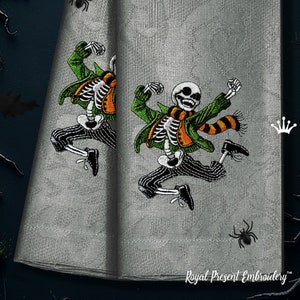 May include: Two embroidered kitchen towels with a skeleton wearing a green jacket and orange and black scarf. The skeleton is jumping in the air with its arms raised. The text "Royal Present Embroidery" is at the bottom of the towels.