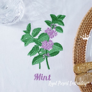 Könnte beinhalten: Gestickte Darstellung eines Minzzweigs mit lila Blüten und dem Wort "Minze" in lila Schrift darunter. Das Design befindet sich auf einem weißen Stoffhintergrund.