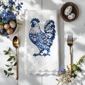 Puede incluir: Toalla de cocina blanca con un diseño de gallo bordado en azul y blanco. El gallo está detallado con patrones florales y tiene un borde de encaje.