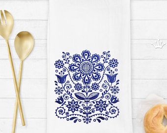 May include: A white kitchen towel with a blue embroidered floral design. The design features a large flower with smaller flowers and leaves surrounding it.
