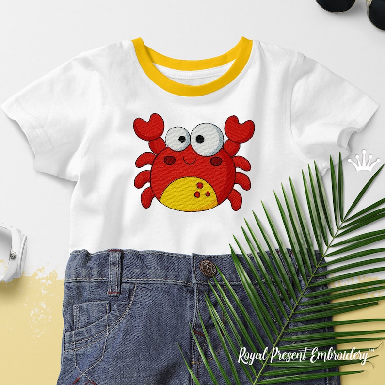May include: A white t-shirt with a yellow trim around the neck. A red cartoon crab with yellow accents is embroidered on the front of the shirt. The crab has large, white eyes and a smiling mouth. The text 'Royal Present Embroidery' is visible at the bottom of the image.