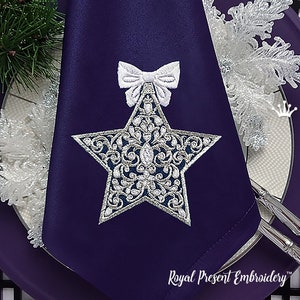 May include: A purple napkin featuring an embroidered silver and white star ornament with a white bow on top. The text "Royal Present Embroidery" is at the bottom of the napkin.