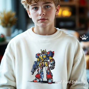 Peut inclure: Un sweat-shirt blanc avec une image brodée colorée d'un robot. Le robot est bleu, rouge, jaune et noir. Le texte "Royal Present Embroidery" est imprimé sous le robot.