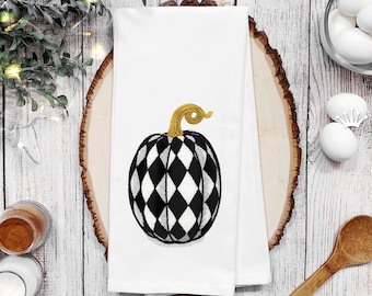 May include: A white kitchen towel with a black and white chequered pumpkin embroidered on it. The pumpkin has a gold stem.