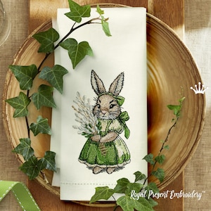 May include: Embroidered design of a brown bunny rabbit wearing a green dress and holding a bouquet of white flowers. The design is on a white linen napkin.
