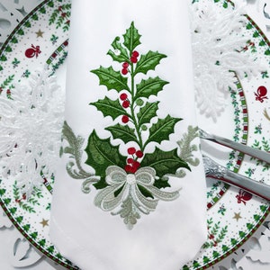 May include: White embroidered napkin with a green holly sprig and red berries, a silver bow, and a decorative scroll design.