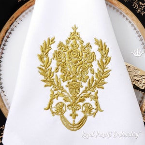 May include: Gold embroidered design featuring a floral bouquet with leaves and a decorative base. The design is on a white fabric background.