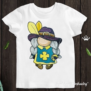 May include: Embroidered design of a gnome wearing a purple hat with a yellow feather, a blue and yellow tunic with a yellow cross, and holding a sword. The gnome has a white beard and is standing on a white t-shirt.