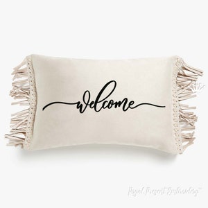 May include: A white cushion with a fringe border and the word "welcome" written in black cursive script.