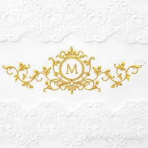 Op de afbeelding: Gouden borduurwerkontwerp met een decoratief frame met de letter "M" in het midden. Het ontwerp is omgeven door sierlijke bloemmotieven.