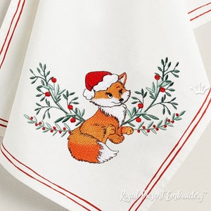 May include: Embroidered design of a fox wearing a Santa hat, surrounded by green leaves and red berries. The design is on a white fabric with red trim.