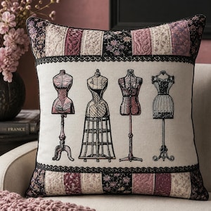 May include: A square throw pillow featuring a central cream-colored panel with black embroidered illustrations of four distinct dress forms. The top and bottom borders consist of a quilted patchwork pattern in shades of black, mauve, and floral.