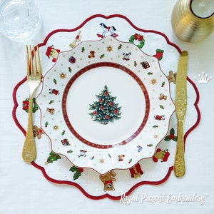 May include: A white porcelain plate with a red and gold border features a Christmas tree design. The plate is on a white embroidered placemat with a red border and a variety of Christmas-themed designs, including toys, a wreath, and holly.