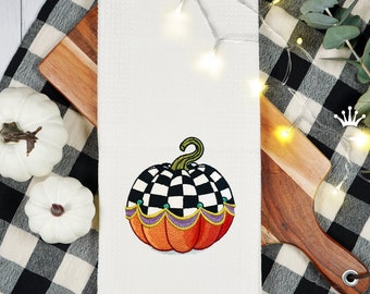 May include: A white kitchen towel featuring an embroidered checkered pumpkin. The pumpkin is orange with black and white checkered accents and a purple and green trim. The towel has a red border and the text "Royal Present Embroidery" is printed in the bottom right corner.