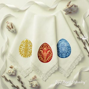 May include: Three white linen handkerchiefs with embroidered Easter egg designs in gold, red, and blue. Each handkerchief has a delicate lace trim. Decorative ceramic bunnies and pussy willow branches are arranged around the handkerchiefs.