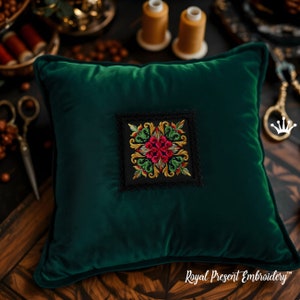 May include: A green velvet pillow with a square embroidered design featuring red and gold flowers on a black background. The pillow is on a wooden surface with spools of thread and other crafting supplies.