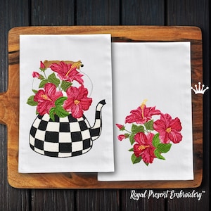Könnte beinhalten: Zwei weiße Geschirrtücher mit gestickten Bildern von rosa Hibiskusblüten. Ein Handtuch zeigt eine schwarz-weiß karierte Teekanne mit Hibiskusblüten darin. Das andere Handtuch zeigt einen Strauß Hibiskusblüten. Die Handtücher werden auf einem Holzbrett präsentiert.