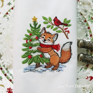 Puede incluir: Diseño bordado de un zorro abrazando un árbol de Navidad con adornos rojos y un cardenal posado en una rama. El zorro lleva una bufanda roja y tiene la punta de la cola blanca.