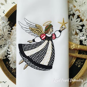 May include: Embroidered angel design on white fabric. The angel has gold and white wings, a gold halo, and is holding a gold star. The angel's dress is black and white with gold accents. The text "Royal Present Embroidery" is at the bottom.