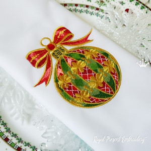 Könnte beinhalten: Gestickter Weihnachtsbaumschmuck mit einer roten Schleife und goldenen Verzierungen. Der Baumschmuck ist grün, rot und gold mit einem karierten Muster. Der Baumschmuck befindet sich auf einem weißen Hintergrund.