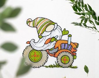 Peut inclure: Broderie représentant un gnome conduisant un petit tracteur orange avec des roues vertes. Le gnome porte un chapeau rayé vert et blanc et a une barbe blanche.