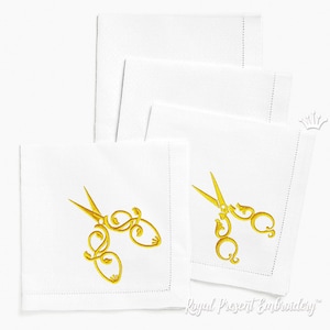 May include: Set of four white linen napkins with gold embroidered scissors. The napkins are folded and stacked on a white surface. The embroidery is detailed and intricate.