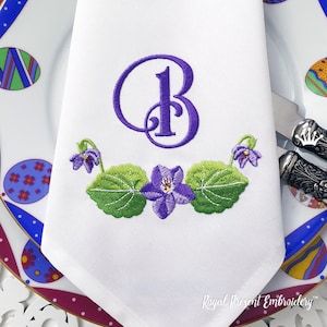 May include: A white linen napkin with a purple embroidered letter "B" and a floral design of green leaves and purple flowers. The text "Royal Present Embroidery" is visible in the bottom right corner.