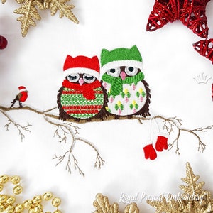 May include: Two embroidered owls wearing winter hats and scarves perched on a snowy branch. The owls are green and red with white accents. A small red bird is perched on the branch behind the owls. The text "Royal Present Embroidery" is visible at the bottom of the image.