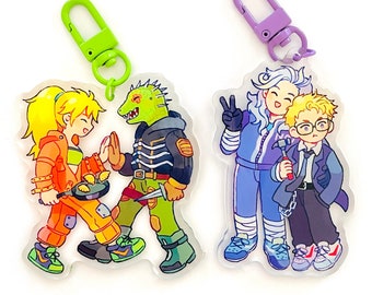 May include: Four colorful cartoon characters on keychains. A green lizard-like creature with a girl in orange overalls, a girl with blue hair and a boy with brown hair. The keychains are made of clear plastic with a metal ring.