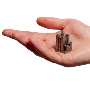 May include: A small, detailed, silver-colored model of a castle with multiple towers and a gate.