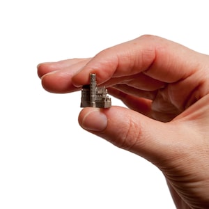 May include: A small, silver-coloured model of a building with a tall spire. The model is being held in a person's hand.