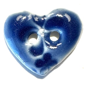 May include: A heart-shaped button with a glossy, deep blue finish. The button has two holes and a white, crackled pattern across its surface. This decorative button is ideal for sewing and craft projects.