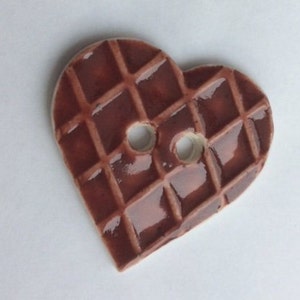 May include: A heart-shaped button with a waffle pattern and two holes. The button is a glossy, dark brown color. This decorative button is suitable for sewing and craft projects.