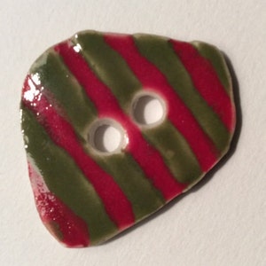 May include: A ceramic button with a unique shape, featuring a glossy finish. The button has two holes and is decorated with alternating red and green diagonal stripes. This decorative button is suitable for sewing and craft projects.