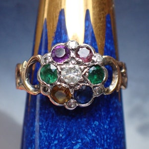 May include: A silver ring with a cluster of colorful gemstones, including a large central diamond, surrounded by smaller diamonds. The ring is set in a gold band.