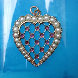 May include: A gold heart-shaped pendant with a delicate lattice design set with pink gemstones and a border of white pearls.