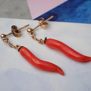 May include: A pair of gold earrings with red coral horn charms hanging from a chain.