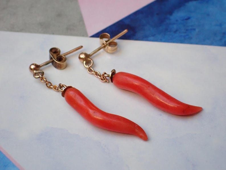 May include: A pair of gold earrings with red coral horn charms hanging from a chain.