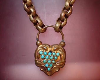 May include: A vintage gold-toned necklace featuring a heart-shaped pendant. The pendant is adorned with turquoise-colored stones and intricate scrollwork. The necklace has a chunky chain design, creating a bold and elegant look.