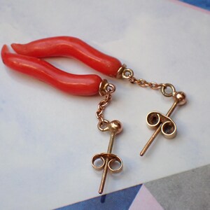May include: A pair of coral earrings with gold chains and posts. The coral is a bright red color and the chains are delicate.