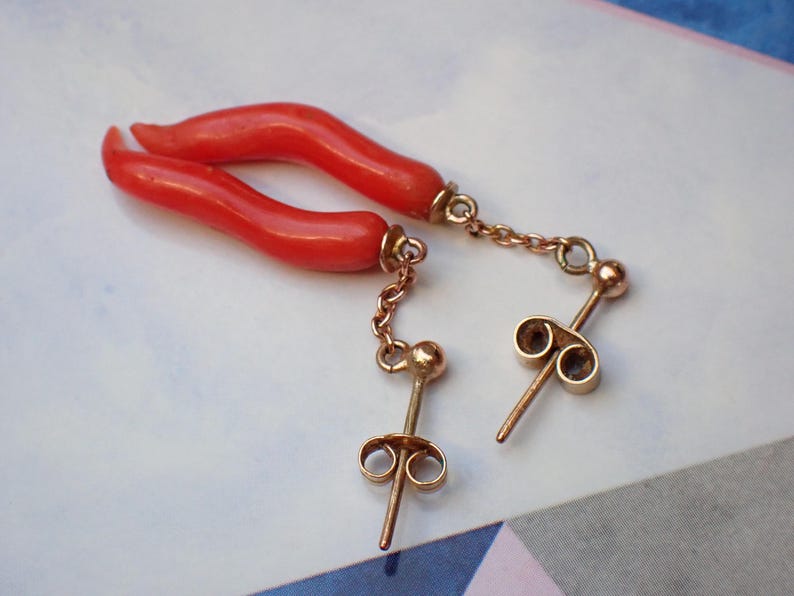 May include: A pair of coral earrings with gold chains and posts. The coral is a bright red color and the chains are delicate.