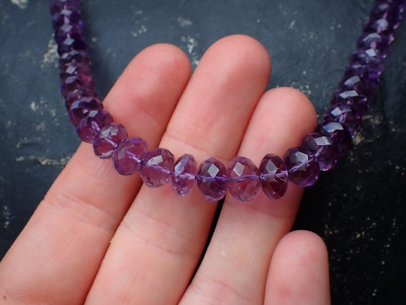 May include: A necklace composed of faceted, deep purple amethyst beads. The beads are strung together, creating a continuous loop. The necklace is displayed against a dark background.