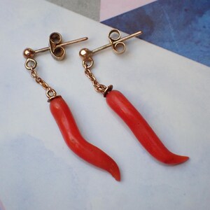 May include: A pair of gold earrings with red coral drop pendants shaped like chili peppers.