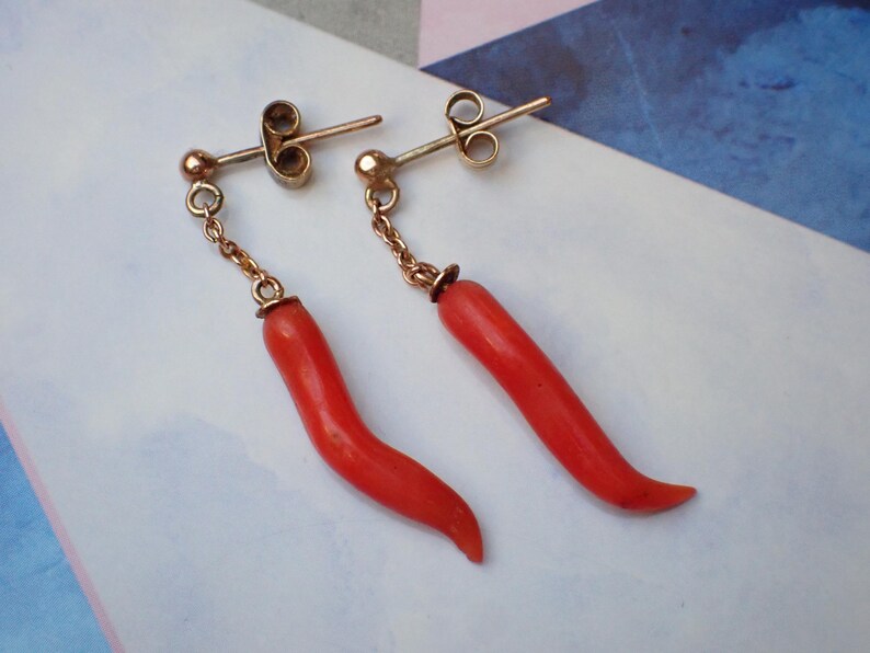 May include: A pair of gold earrings with red coral drop pendants shaped like chili peppers.