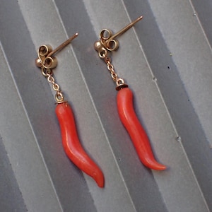 May include: A pair of gold earrings with red coral pendants shaped like chili peppers.