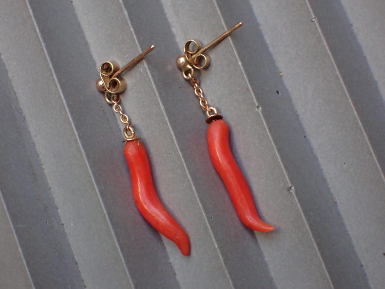 May include: A pair of gold earrings with red coral pendants shaped like chili peppers.