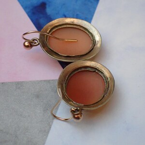 May include: A pair of antique gold tone earrings with a cameo design. The cameos are oval shaped and feature a pink colored design.