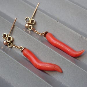 May include: A pair of coral earrings with gold accents. The coral is a bright red color and is shaped like a curved horn. The earrings are attached to a gold chain.