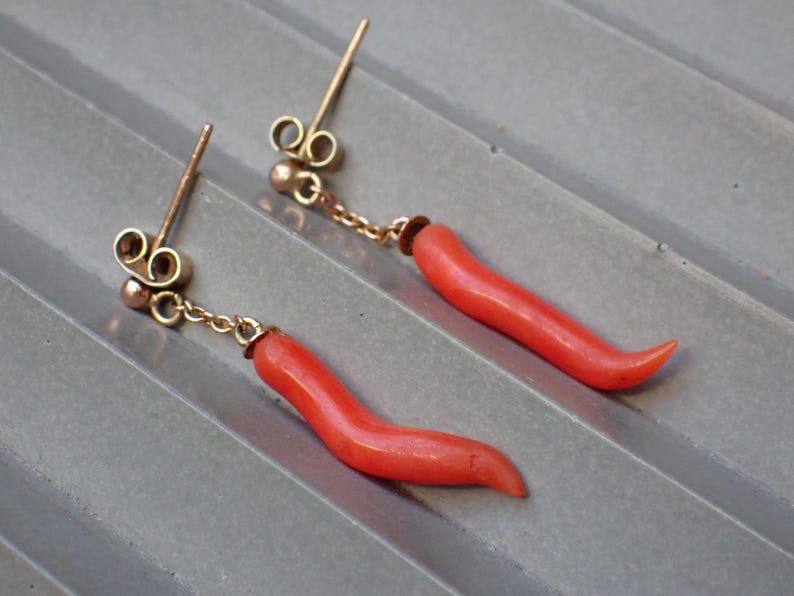 May include: A pair of coral earrings with gold accents. The coral is a bright red color and is shaped like a curved horn. The earrings are attached to a gold chain.
