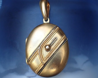 May include: A gold oval locket with an intricate design. The locket has a hinged lid and a loop for a chain.